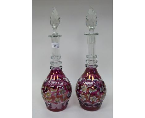 A pair of 20thC part gilt painted, cranberry cut glass, bulbous decanters with triple ring necks and stoppers