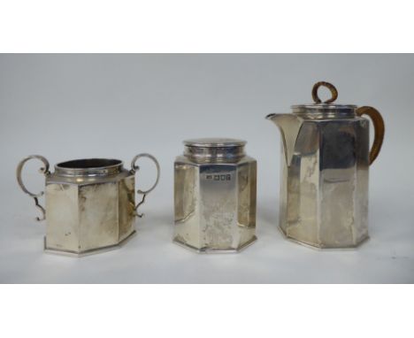 A three piece silver tea set of octagonal form, comprising a hot water pot with a high spout, hinged lid, split cane covered 