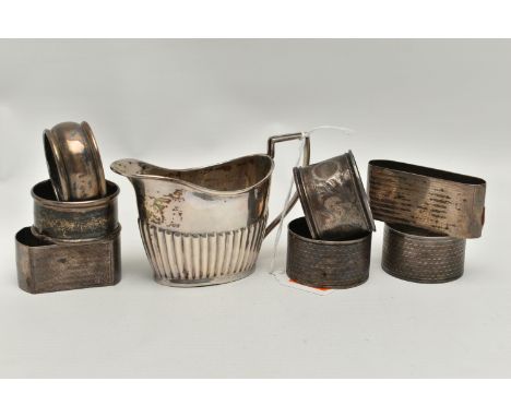 A LATE VICTORIAN SILVER CREAM JUG AND SEVEN ASSORTED SILVER NAPKIN RINGS, the oval cream jug with stop reeded decoration, eng