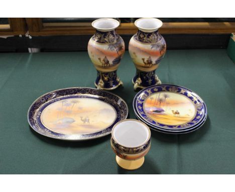 A pair of Noritake vases painted with camels in the desert, 24.5cm high, a similar oval dish, 32.5cm wide, three similar plat