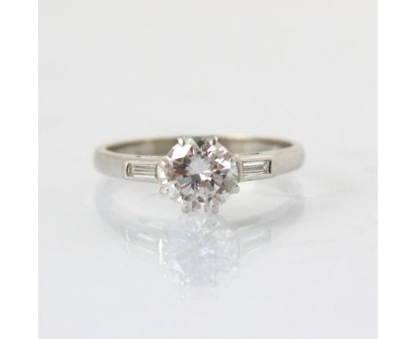 A mid 20th century diamond solitaire ring, the round cut diamond within white metal eight claw setting edge, with baguette cu