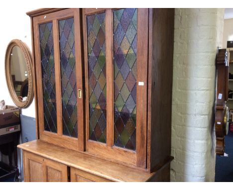 An oak wall unit with sliding panel doors to base with sliding stained glass doors to top sections.
