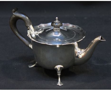 An Edwardian silver small teapot, of cylindrical form with shaped rim raised on three pad feet, with ebonised finial and scro