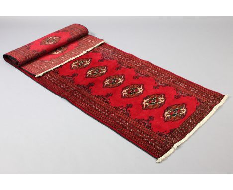 A Turkoman runner of madder ground with central row of fourteen guhls within multiple narrow borders, 80cm x 280cm.