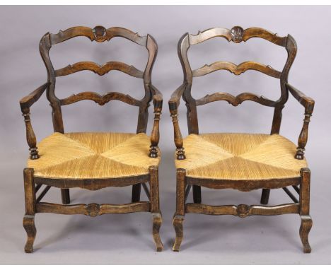 A pair of 19th century French provincial oak low armchairs with carved shell crests to the shaped ladder-backs, with open arm