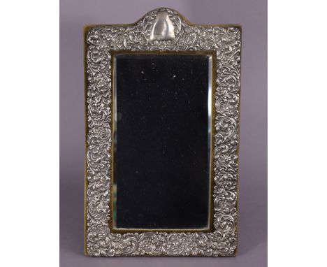 An Edwardian silver table mirror with easel support inset rectangular bevelled plate, the wide border embossed with flowers &