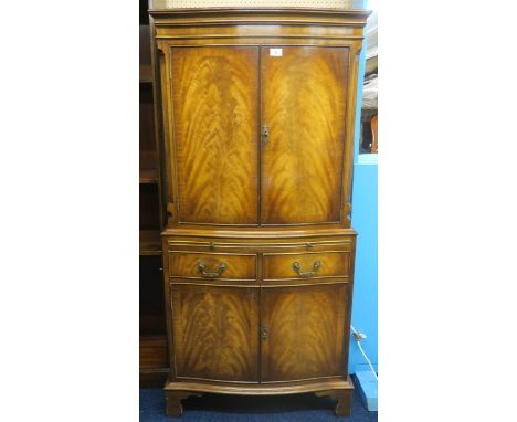 A 20th century mahogany veneered bow front drinks cabinet with pair of cabinet doors concealing mirror lined cocktail compart