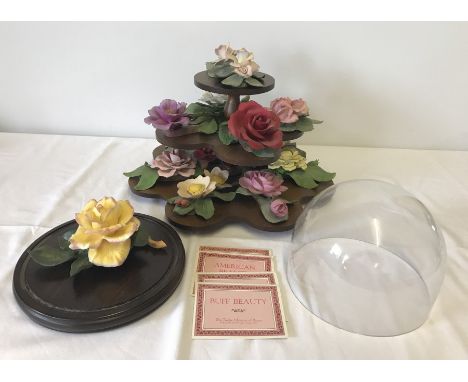 A collection of ceramic rose figurines made by Capodimonte "The Twelve months of Roses" (some a/f). On a wooden stand togethe