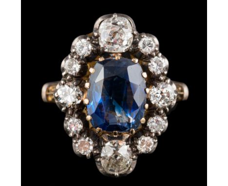 A sapphire and diamond ring: the central oval cut sapphire claw set within a surround of old cut diamonds, in a pierced scrol