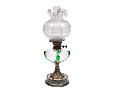 An Art Nouveau period oil lamp:  with clear and green glass overlay reservoir on a waisted brass stem and circular pottery ba