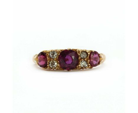 An 18ct gold three stone carved head ring,a round mixed cut ruby to the centre, flanked by an oval cut ruby and an oval cut g