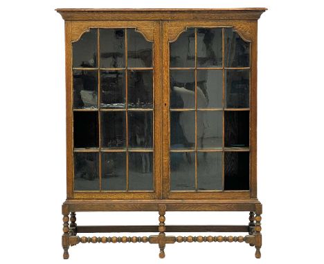 An oak display cabinet or bookcase. Circa 1920, with two glazed doors, on reel and bobbin turned legs and stretcher, height 1