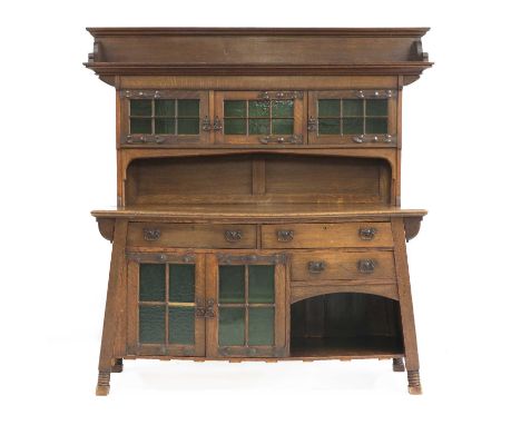 An Arts and Crafts oak dresser,by Goodyers, in two parts with glass mounted cupboards, over drawers and cupboards, with a wel