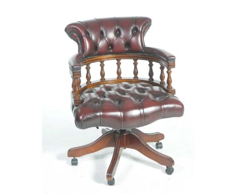 An oxblood red leather revolving captains chairWith a button back above padded out swept arms raised on turned spindles over 