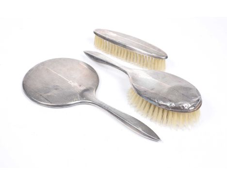 A silver three piece dressing table set Comprising silver back hand mirror, hairbrush, and clothes brush, with engine turned 