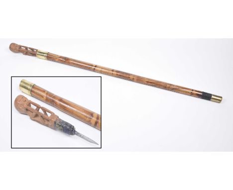 A late 19th Century bamboo walking stick, with concealed dagger handle The carved wooden top depicting a seated abstract figu