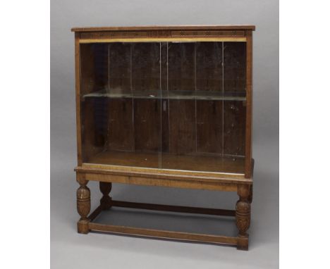 AN INLAID OAK BOOKCASE, dated 1925 with geometric inlay to the frieze, glass sliding doors and interior shelf, on carved bulb