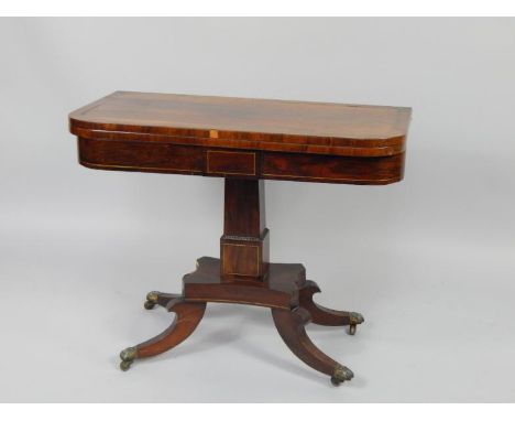 A Regency rosewood and brass inlaid fold over card table, raised on a square column, above a quatrefoil base and scrolling le