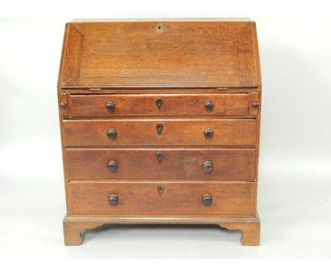 A George III oak bureau, the fall flap opening to reveal shaped drawers and recesses, over four long graduated drawers, raise