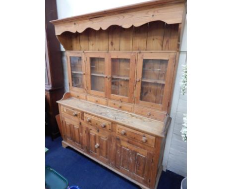 A pine dresser, the shaped pediment over a delft rack with four glazed doors above drawers, over three drawers and cupboards 