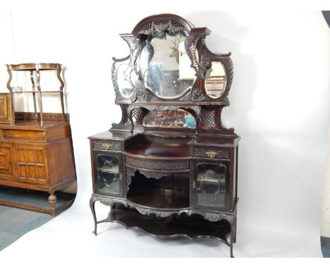 A Victorian mahogany display cabinet, the domed pediment over a pierced and foliate carved superstructure, with a four bevell