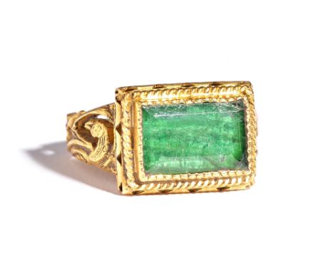 A gold ring, mounted with a close backed rectangular cut emerald, the shoulders decorated with birds, the bezel having a cabl