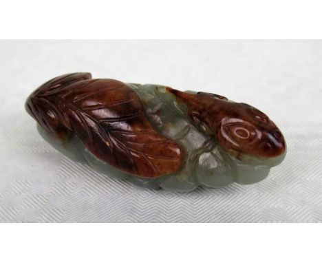 A celadon jade netsuke depicting a stylized amphibian beside a leaf, 6cm wide.