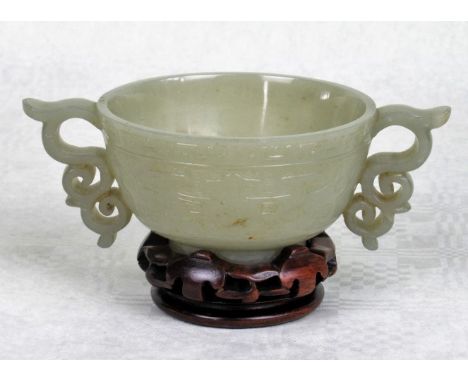 A Chinese pale celadon jade libation cup, the twin handles of scroll form, the body with finely carved stylized motif decorat