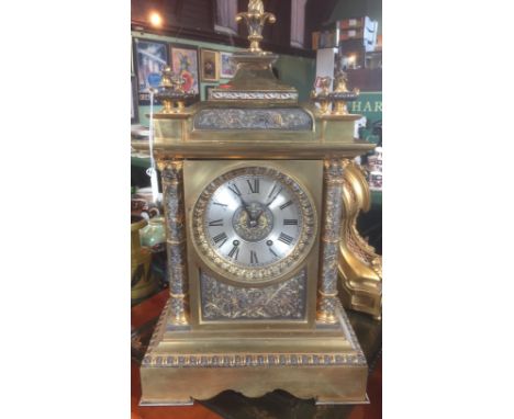 A large late 19th century gilt brass mantle clock, having flame finials over a silvered chapter ring bearing Roman numerals, 