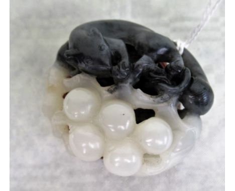 A Chinese two-colour jade netsuke modelled as an animal with a bunch of grapes, 4.6cm wide, on circular wooden display stand.