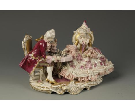 A GERMAN PORCELAIN GROUP of a lady and gentleman playing chess, seated on gilt rococo chairs on a rococo base, 6" high