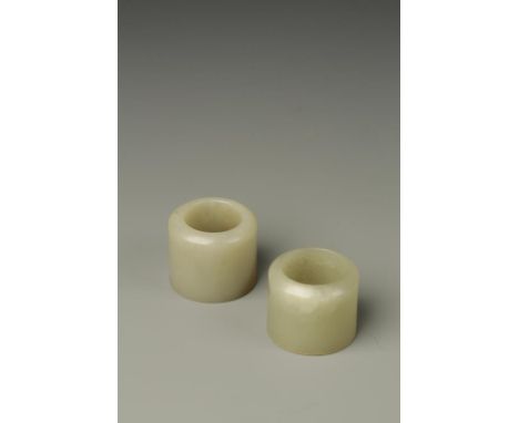 TWO CHINESE CELADON JADE ARCHERS RINGS, one with a russet area, late Qing, 1.25" dia. (2)