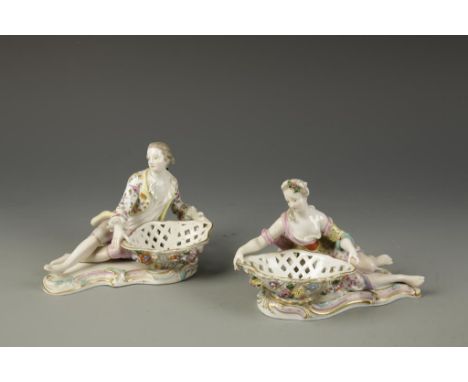 A PAIR OF MEISSEN TABLE SALTS with a man and woman, each holding a basket encrusted with flowers, on a scrolled rococo base, 