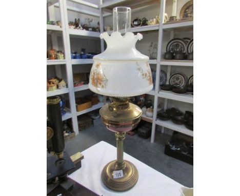 A brass oil lamp with floral decorated shade
