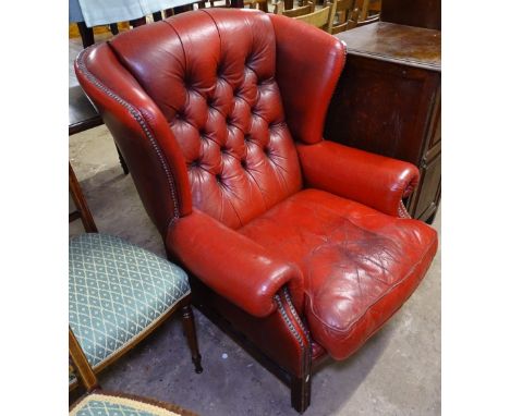 A studded button-back red leather upholstered fireside wing-back chair 