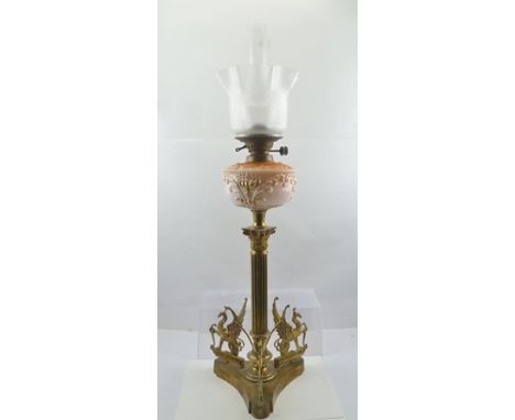 A LATE VICTORIAN OIL LAMP having pink glass reservoir, on brass Corinthian column stem, the base mounted with three griffins,