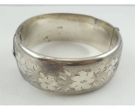 A BROAD SILVER BANGLE with engraved Victorian design decoration 