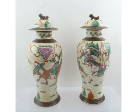 A PAIR OF JAPANESE CERAMIC VASES AND COVERS, of baluster form, crackle ground painted with warriors in landscape, 27cm high 
