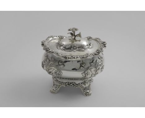 AN EARLY VICTORIAN TEA OR SUGAR CADDY of bombe form with embossed floral decoration, a border of floral scrolls and four curv