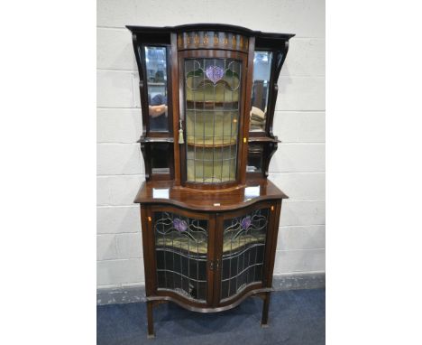 AN ARTS AND CRAFTS MAHOGANY AND MARQUETRY INLAID SERPENTINE DISPLAY CABINET, the top with beveled mirror plates and shelf fla