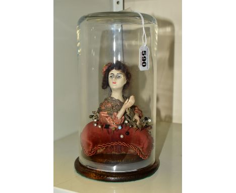A PINCUSHION IN THE FORM OF A WOMAN, with chalkware head and ceramic lower arms, on a square cushion holding thirty six pins,