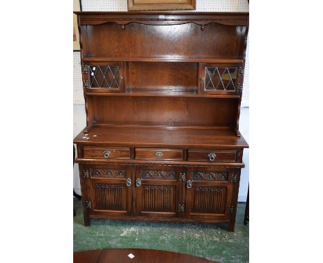 An Old Charm oak dresser, two lead glazed cupboards and shelving to top, three short drawers over three linen fold panel door