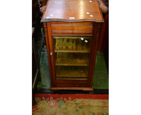 An oak music cabinet, serpentine top, glazed door enclosing lined shelf