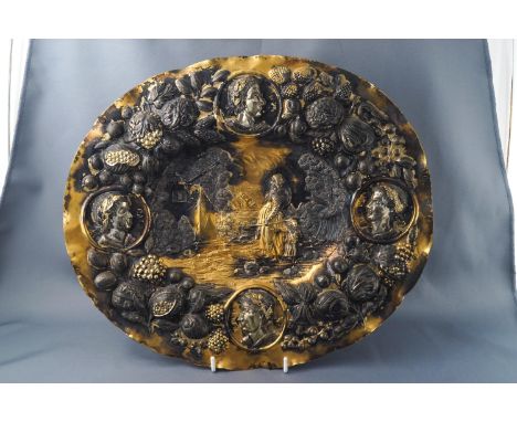 A 19th century continental gilt oval dish with repousse decoration, the centre with figures in a landscape, the rim with four