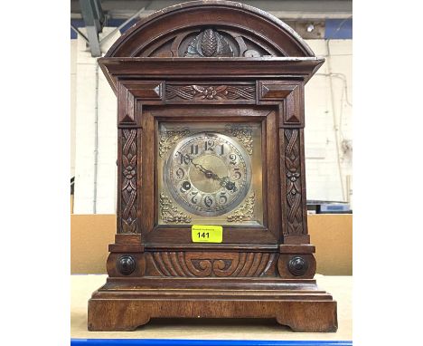 A mantel clock in carved oak case with brass dial and bevelled glass arch top, striking movement 