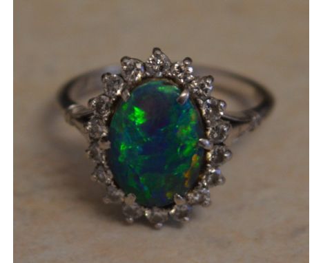 18ct white gold black opal and diamond cluster ring, central oval black opal of good colour, mainly greens &amp; blues, surro