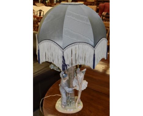 A Lladro figural lamp decorated with a clown and a ballerina dancing around a tree, with blue silk shade, 75cm (including sha