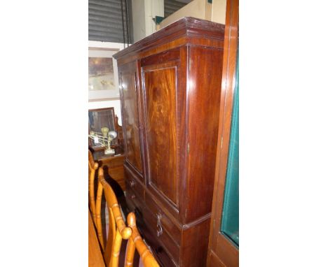 A William IV mahogany linen press the shaped corner above panel doors enclosing sliding trays with drawers below on bracket f