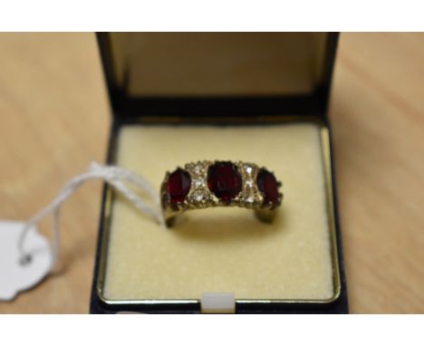 A yellow metal three stone ring, the three graduated oval cut red paste interspersed with four clear stones, on a shank marke