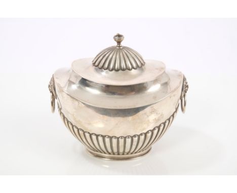 Edwardian silver tea caddy of oval half-fluted form, with twin lion mask ring handles, hinged domed and fluted cover with urn